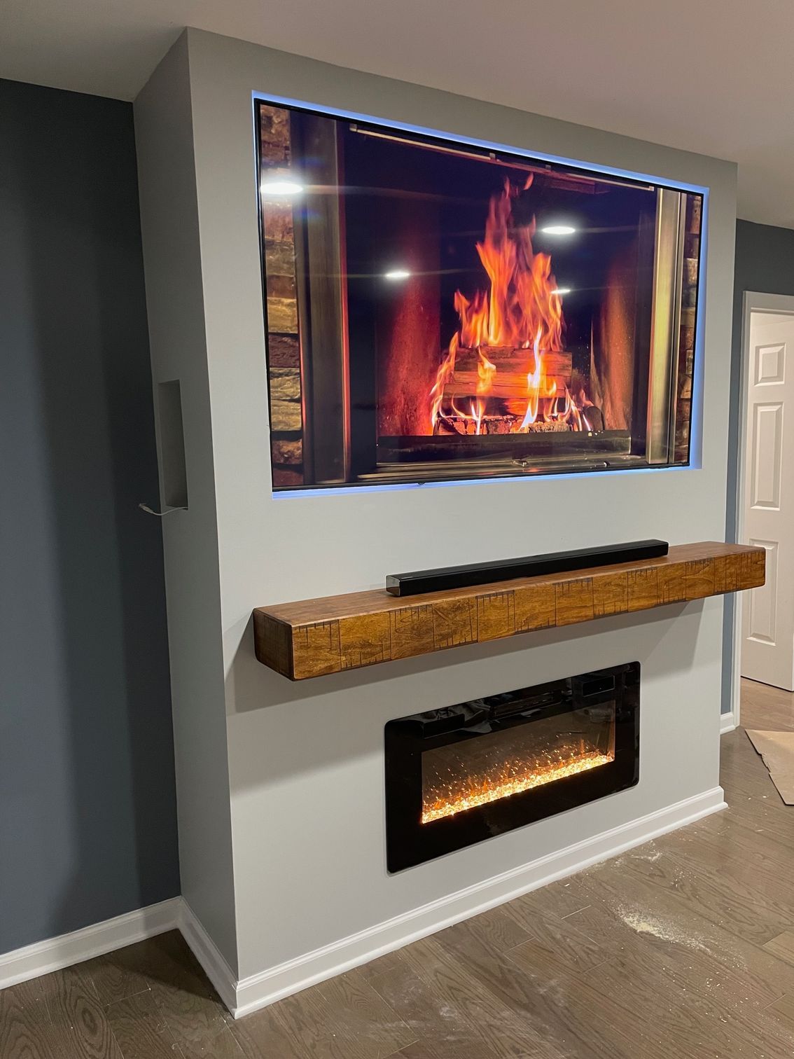Fireplace wall with TV above, wooden mantel, electric fireplace below. Gray wall, cozy setting.