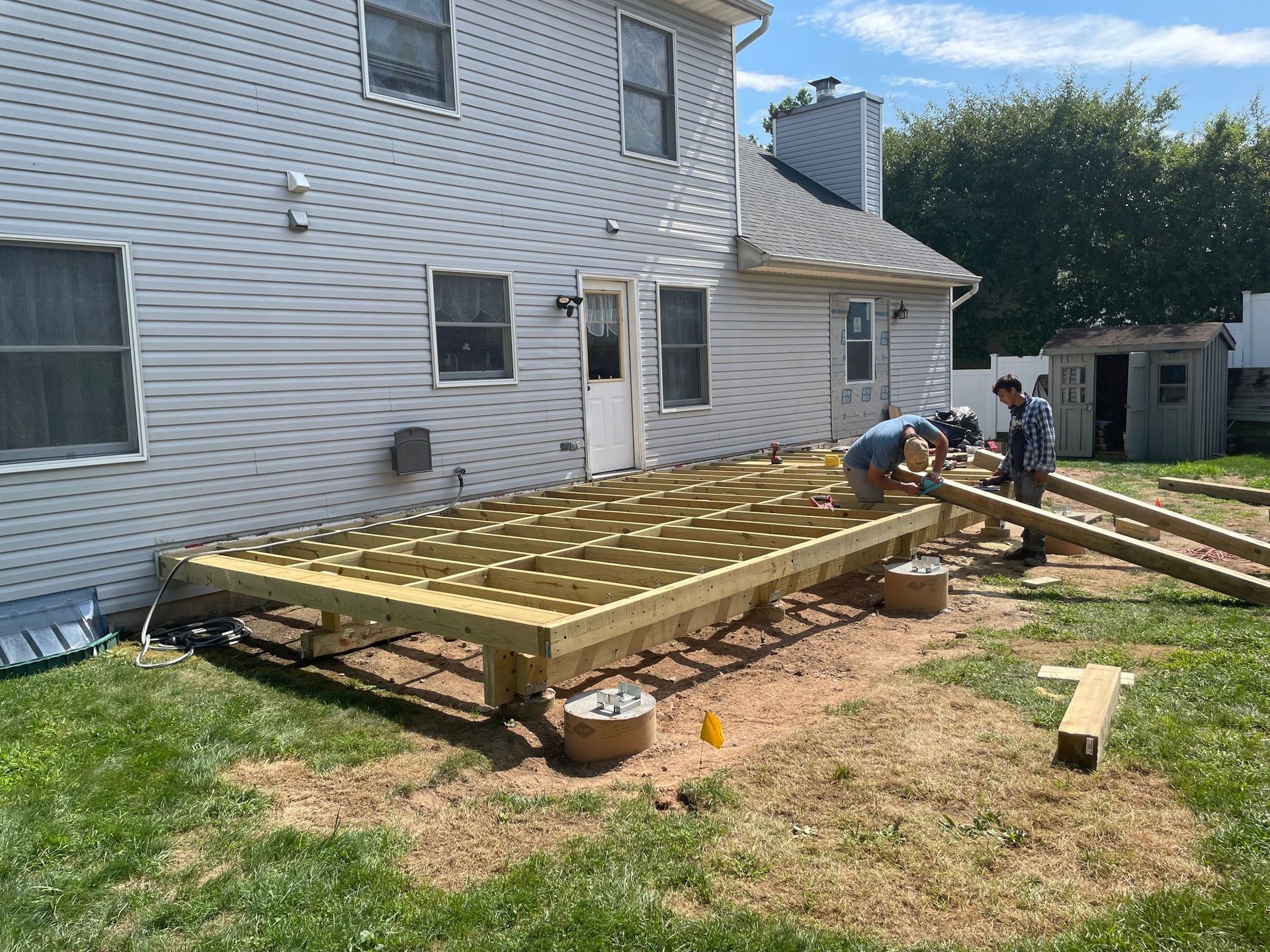 Construction of a wooden deck in a backyard; two people work, bright sunlight.