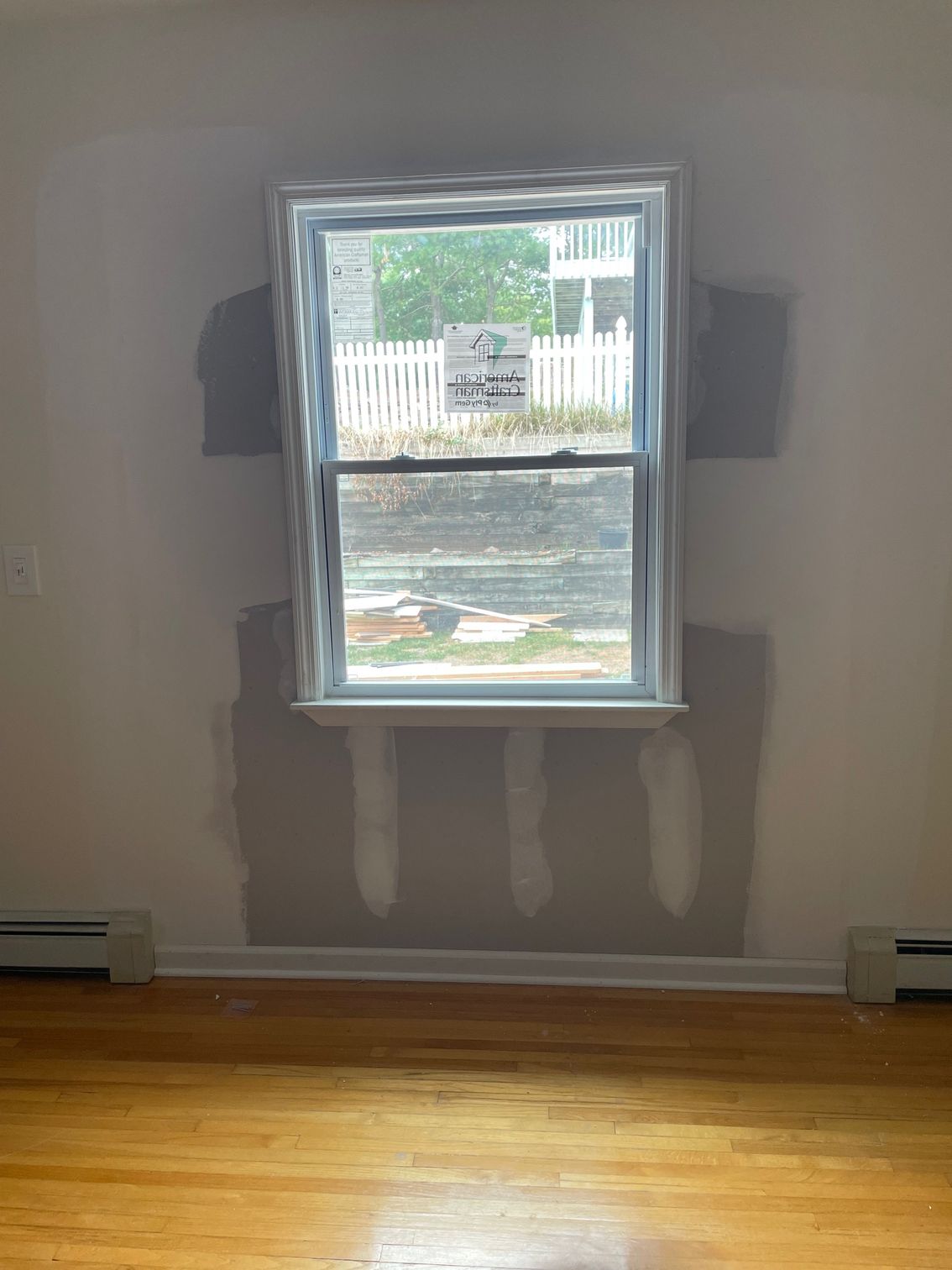 A window installed in a room, surrounded by gray wall patching on a light beige wall.