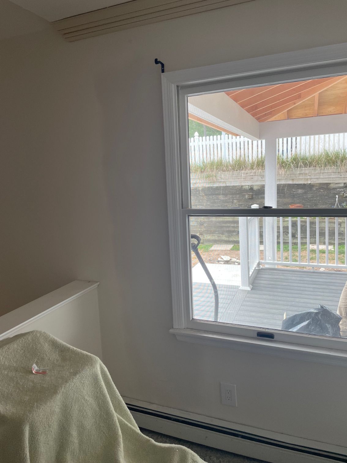 White room with a window overlooking a backyard deck, a curtain rod, and a wrapped table.