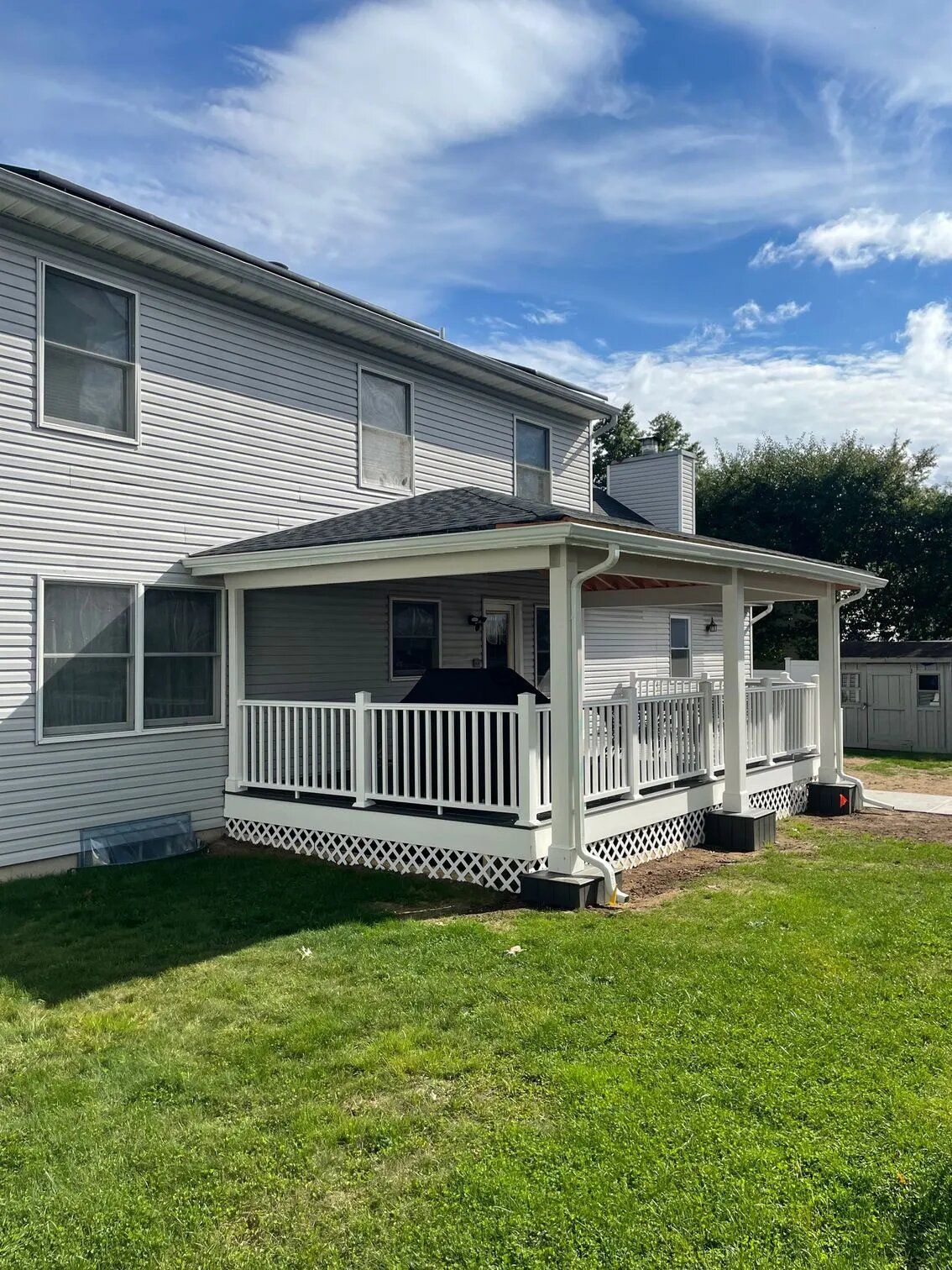 Two-story house with a white porch; the sky is blue with scattered clouds. Green lawn in front.