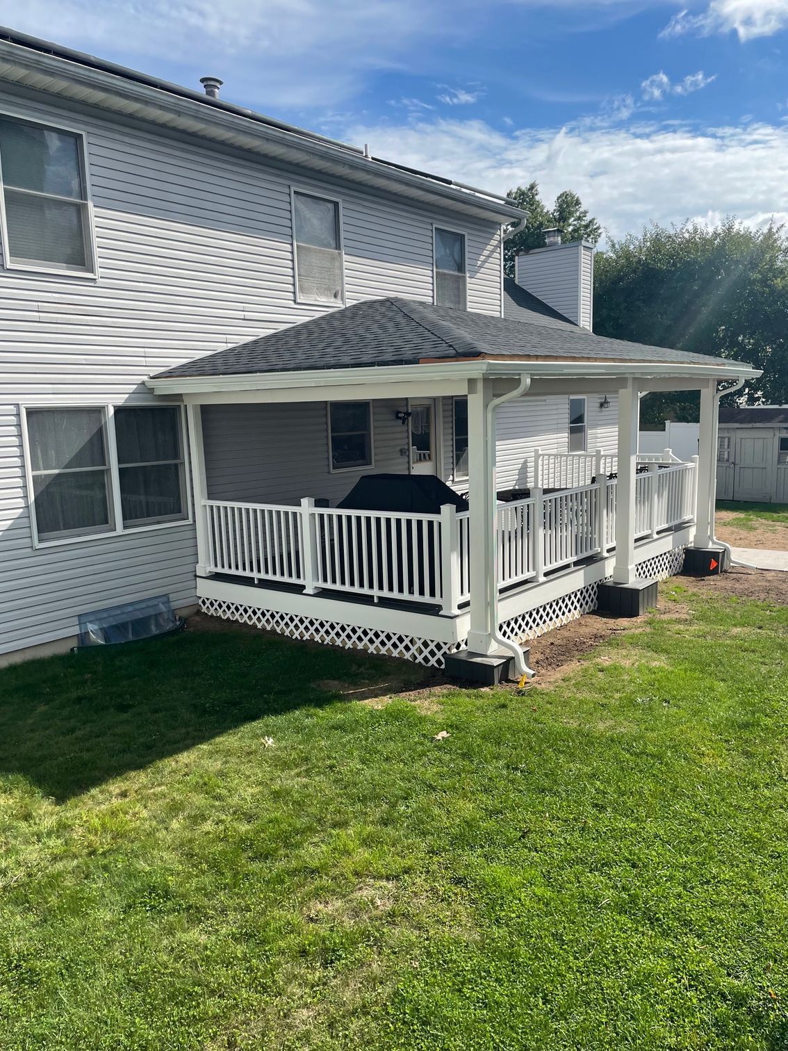 White deck with a dark roof, attached to a light-colored house on a grassy lawn under a blue sky.