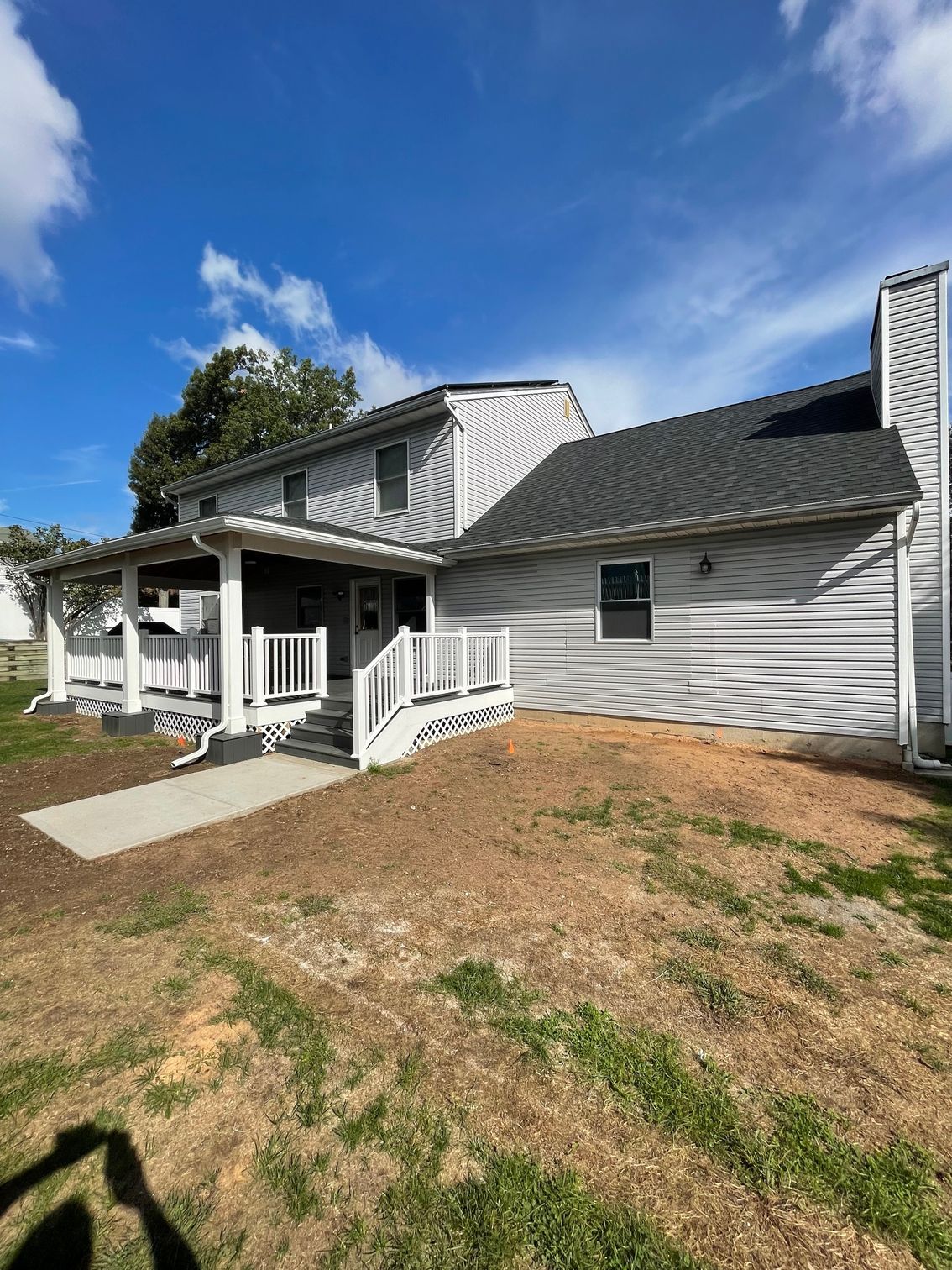 Two-story house with light grey siding, white porch, and a clear blue sky.