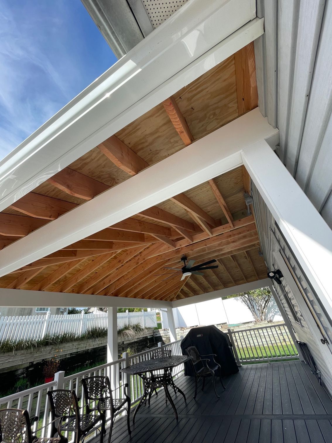 Porch ceiling with curved wooden panels, white trim, and a ceiling fan over a deck with furniture.