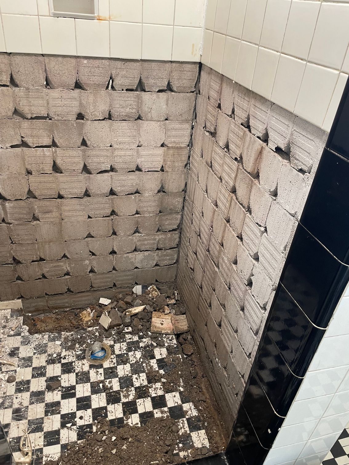 Bathroom with demolished tile wall, checkerboard floor. Debris on the floor.