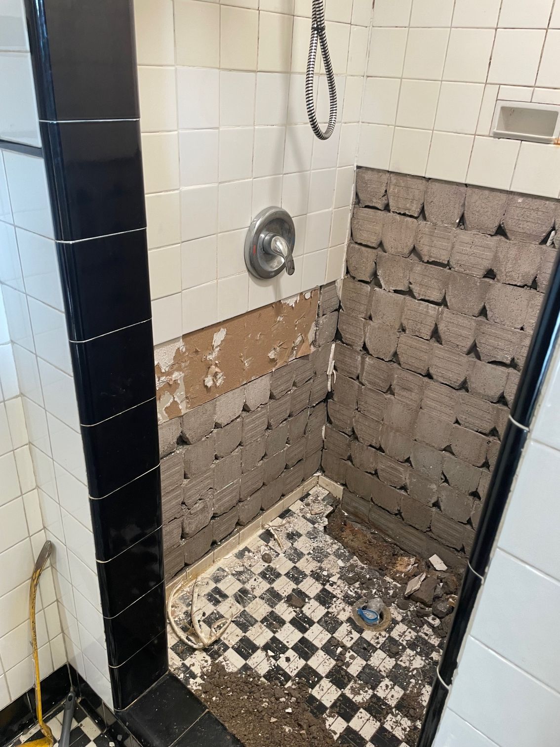 Shower renovation: walls with missing tiles, showing exposed backing, black and white tile floor.