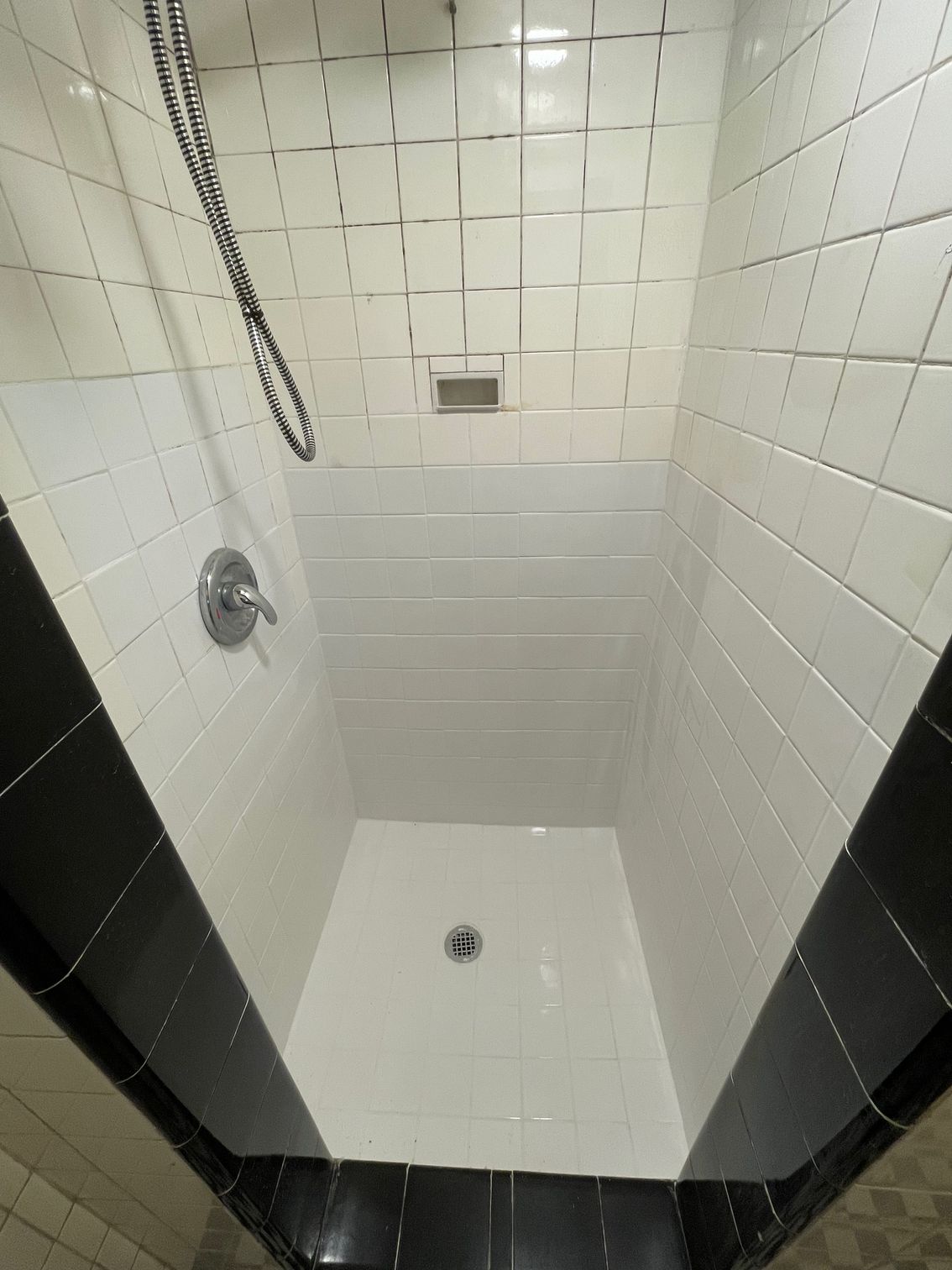 White and black tiled shower with silver fixtures, drain, and shower head.