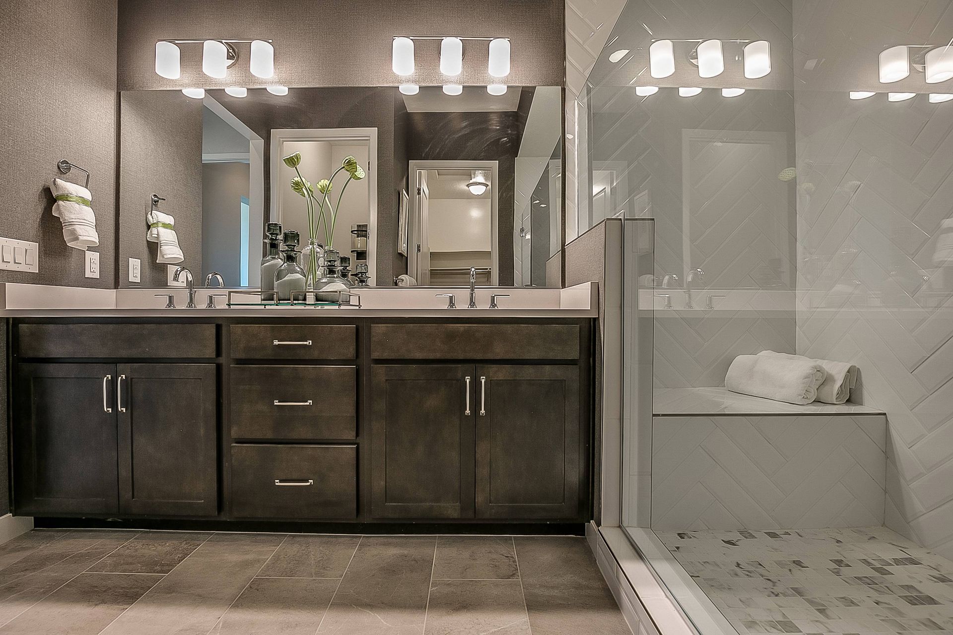 Modern bathroom with dark wood cabinets, large mirrors, and a glass shower.