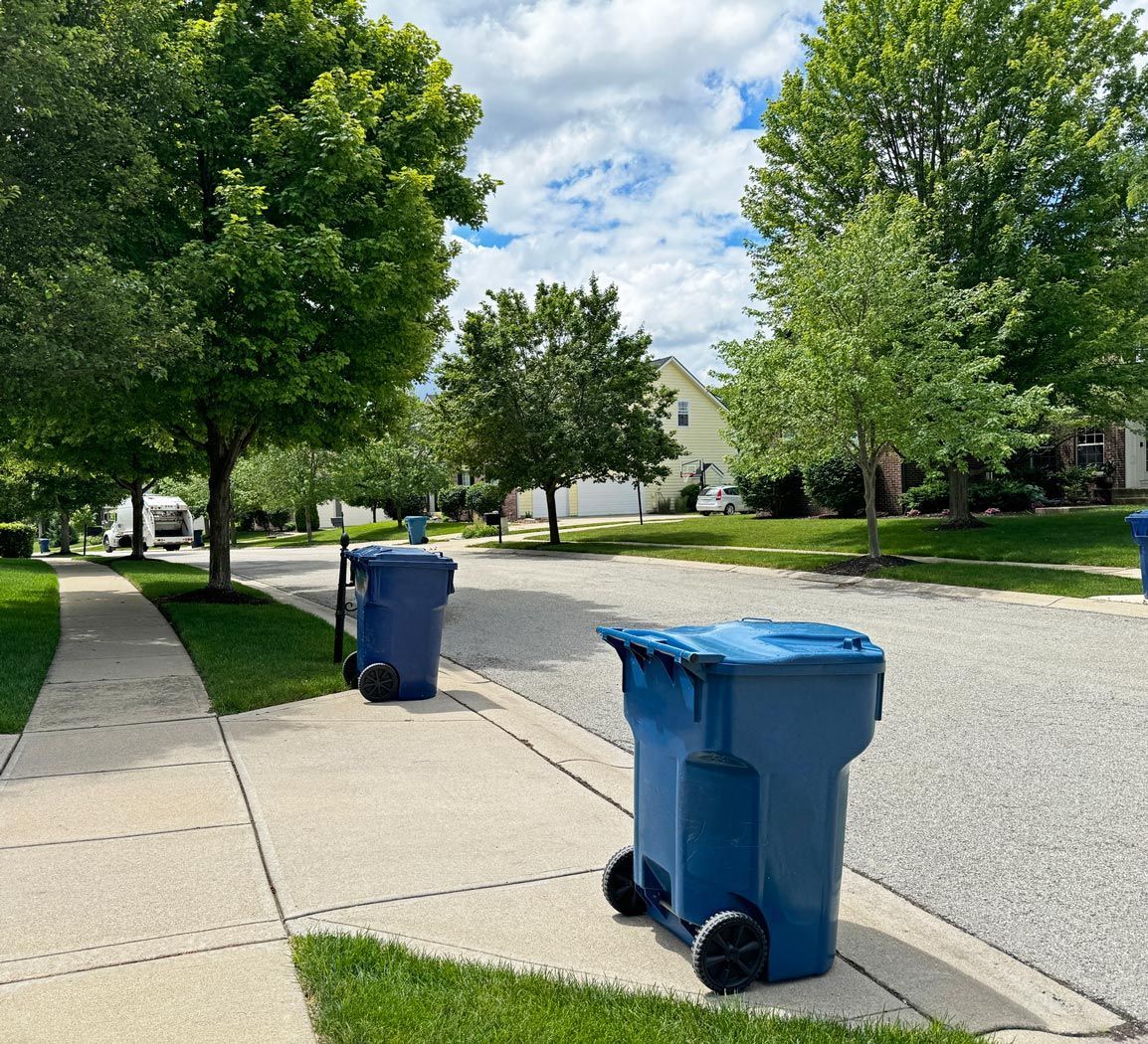 Two blue garbage cans are parked on the sidewalk in a residential neighborhood