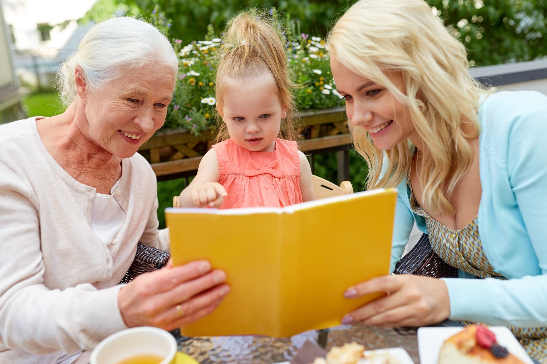 Three people looking at a book: an older person, a young child, and a younger adult, outdoors.