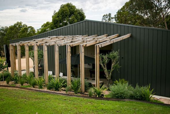A black building with a wooden pergola on the side of it.