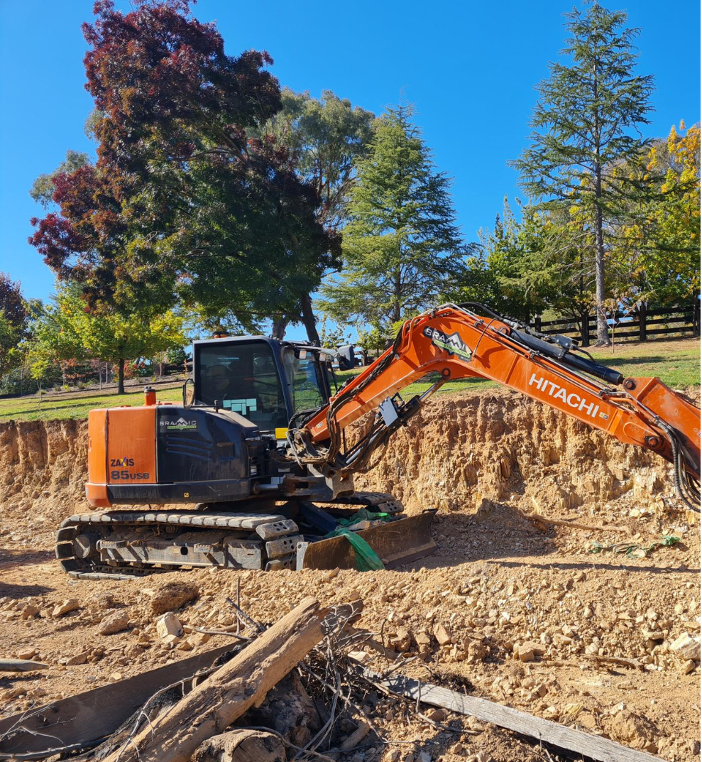 A yellow excavator is sitting on top of a pile of gravel.