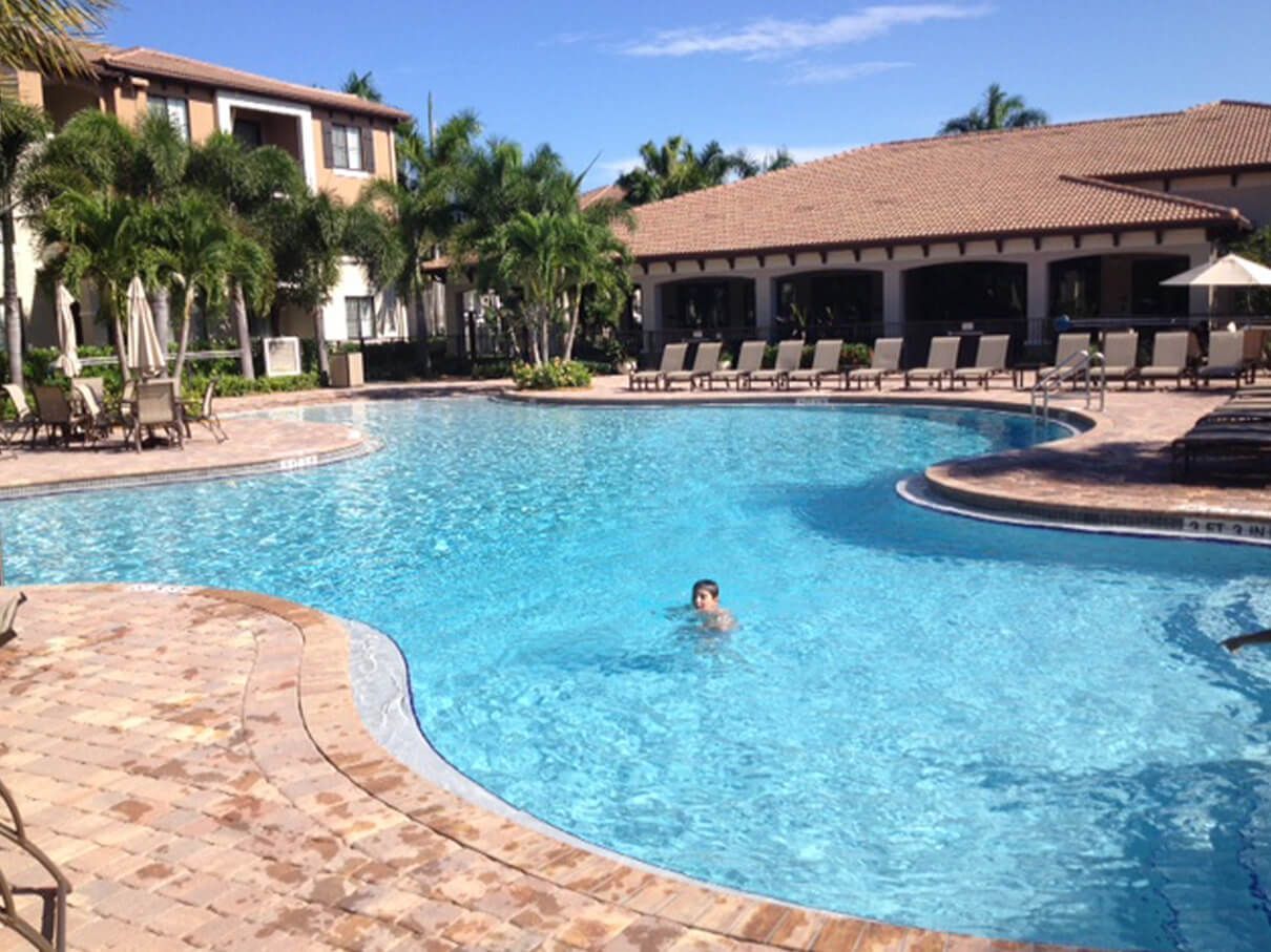 A man is swimming in a large swimming pool surrounded by chairs.