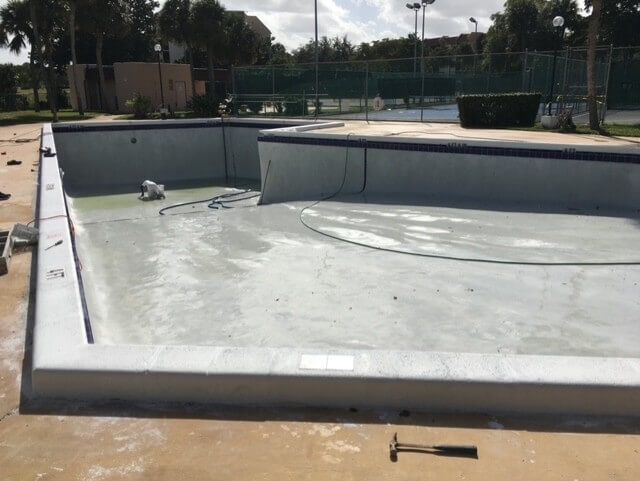 An empty swimming pool with a hammer on the ground next to it.