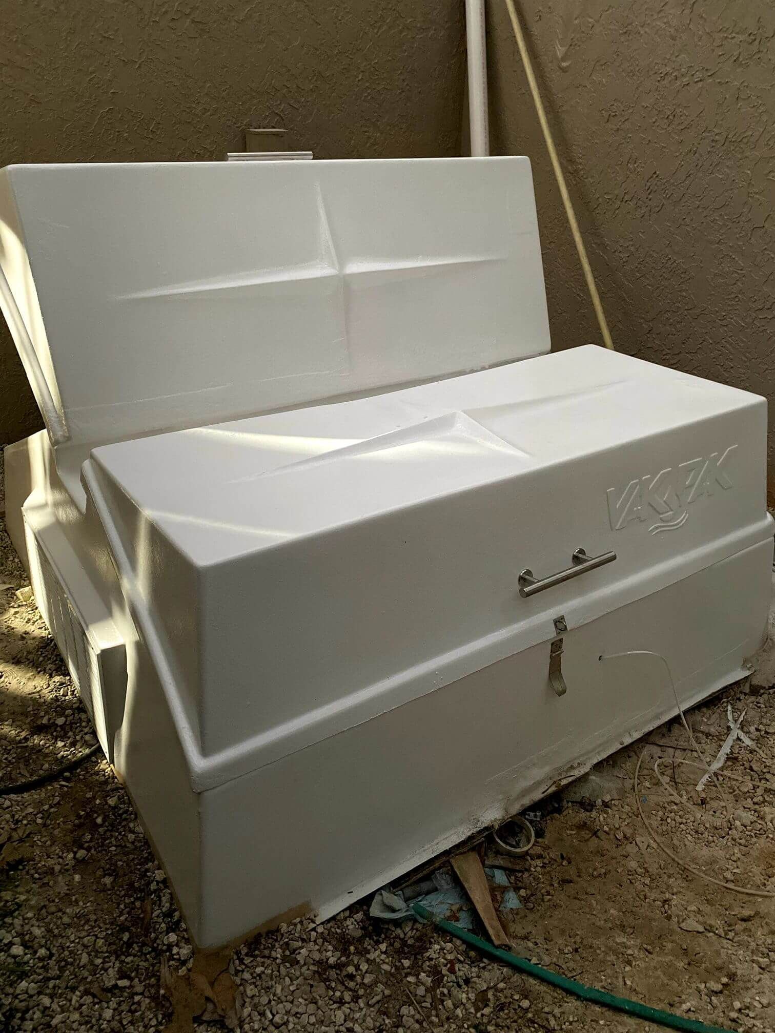 A white box is sitting on the ground next to a hose.