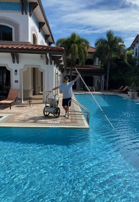 A man is standing next to a swimming pool holding a long pole.