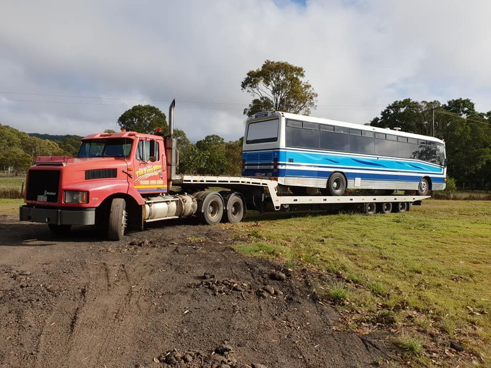 A Red Truck is Towing a Blue and White Bus on a Flatbed Trailer — Hervey Bay Tilt Tray Hire In Takura, QLD