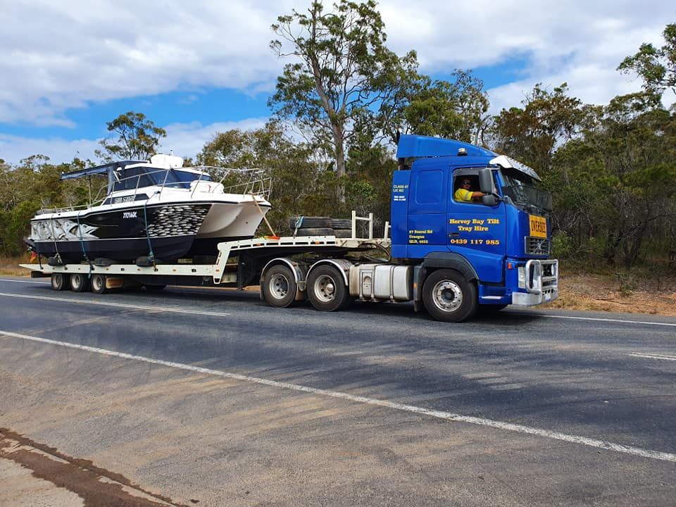 A Blue Truck is Carrying a Boat Down the Road — Hervey Bay Tilt Tray Hire In Takura, QLD