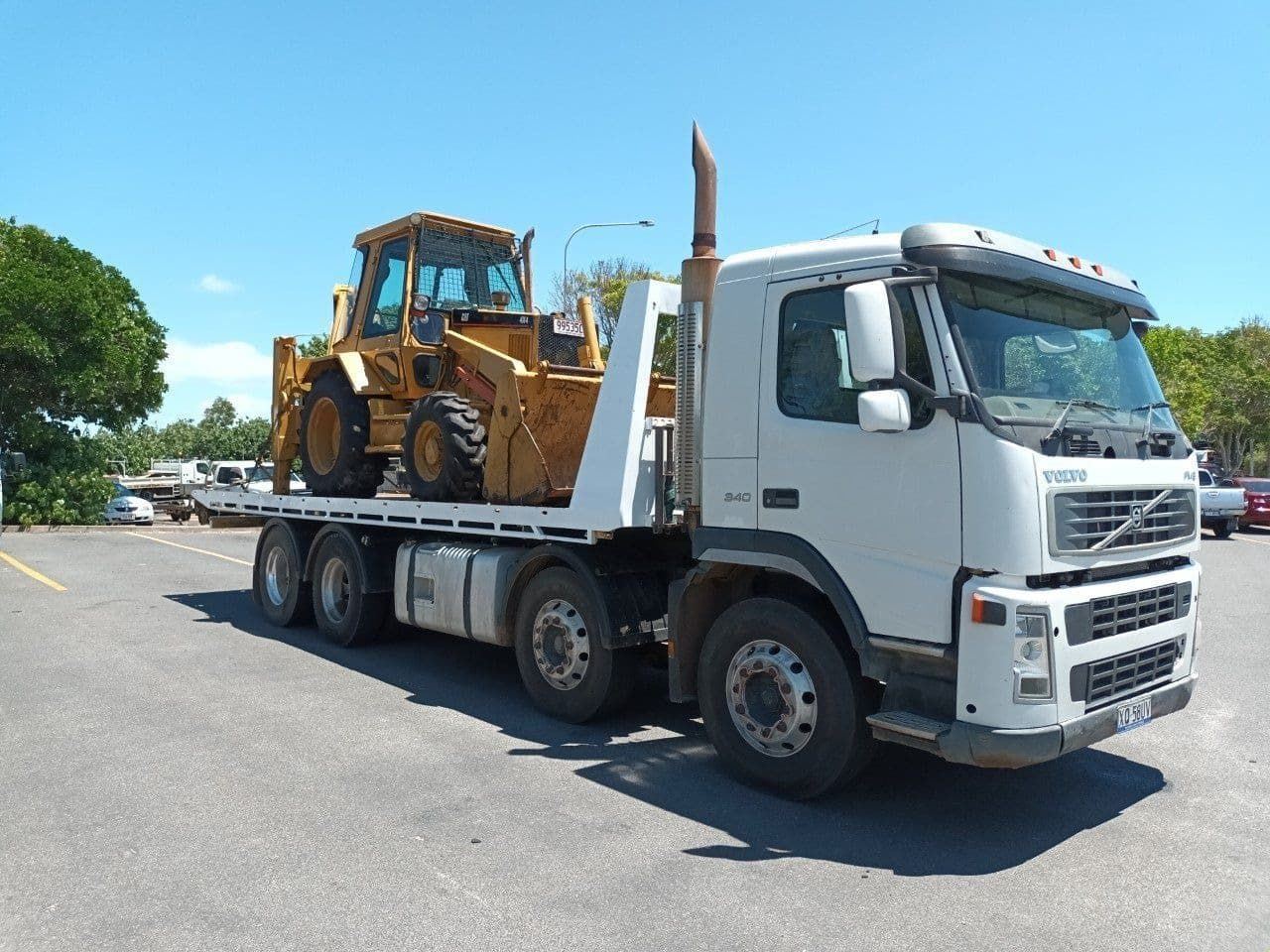 A White Truck With a Bulldozer on the Back is Parked in a Parking Lot — Hervey Bay Tilt Tray Hire In Takura, QLD
