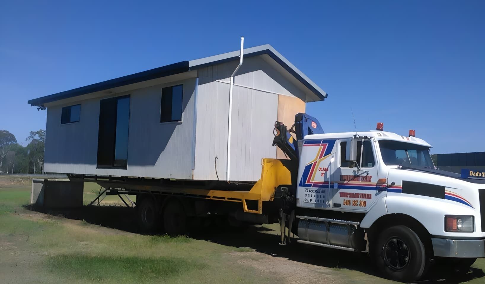 A White Truck is Carrying a Small House — Hervey Bay Tilt Tray Hire In Takura, QLD