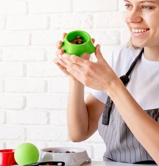 A woman in an apron is holding a green bowl with food in it.