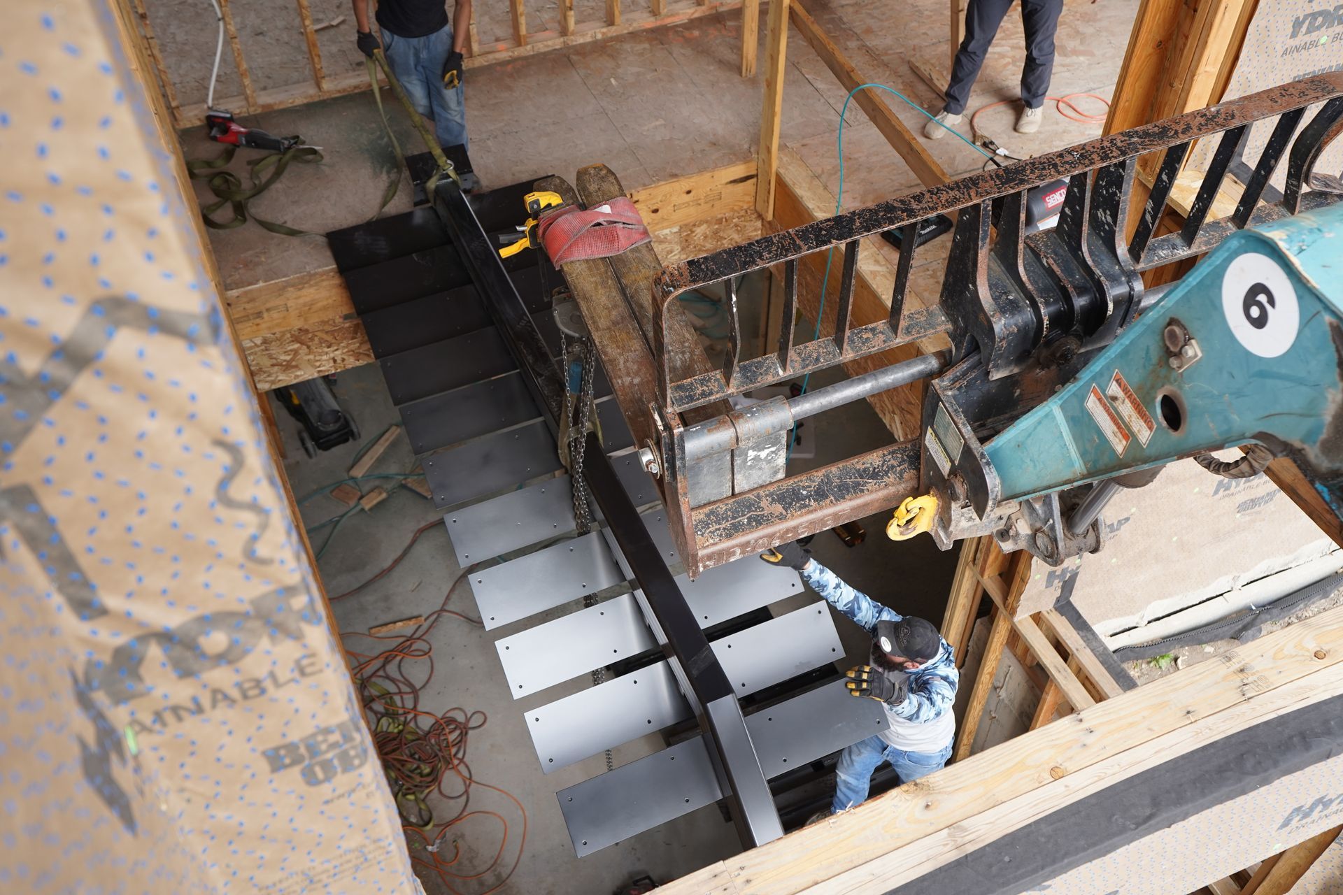Workers using a crane to install black stair treads in an indoor construction site