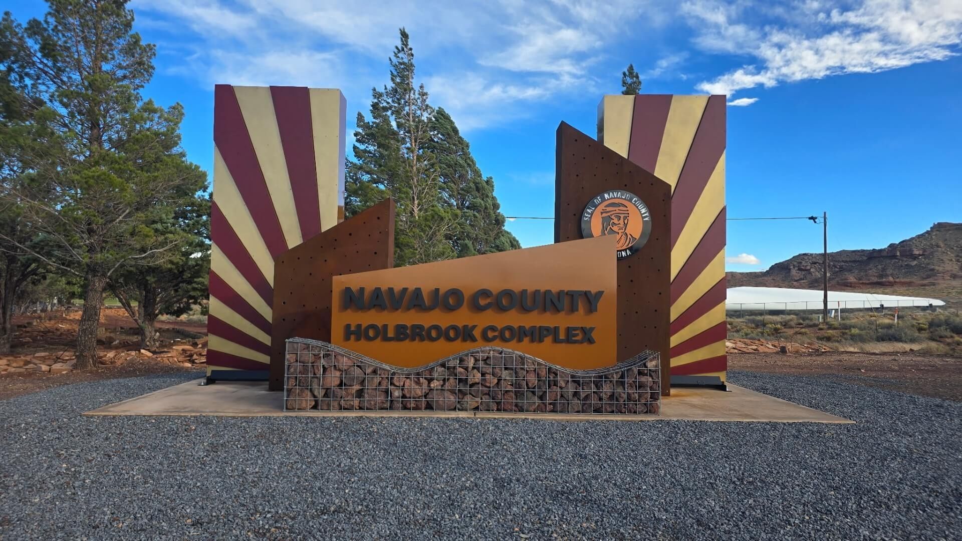 Mojave County Holbrook Complex sign with sunburst pillars, set in a desert landscape under a blue sky