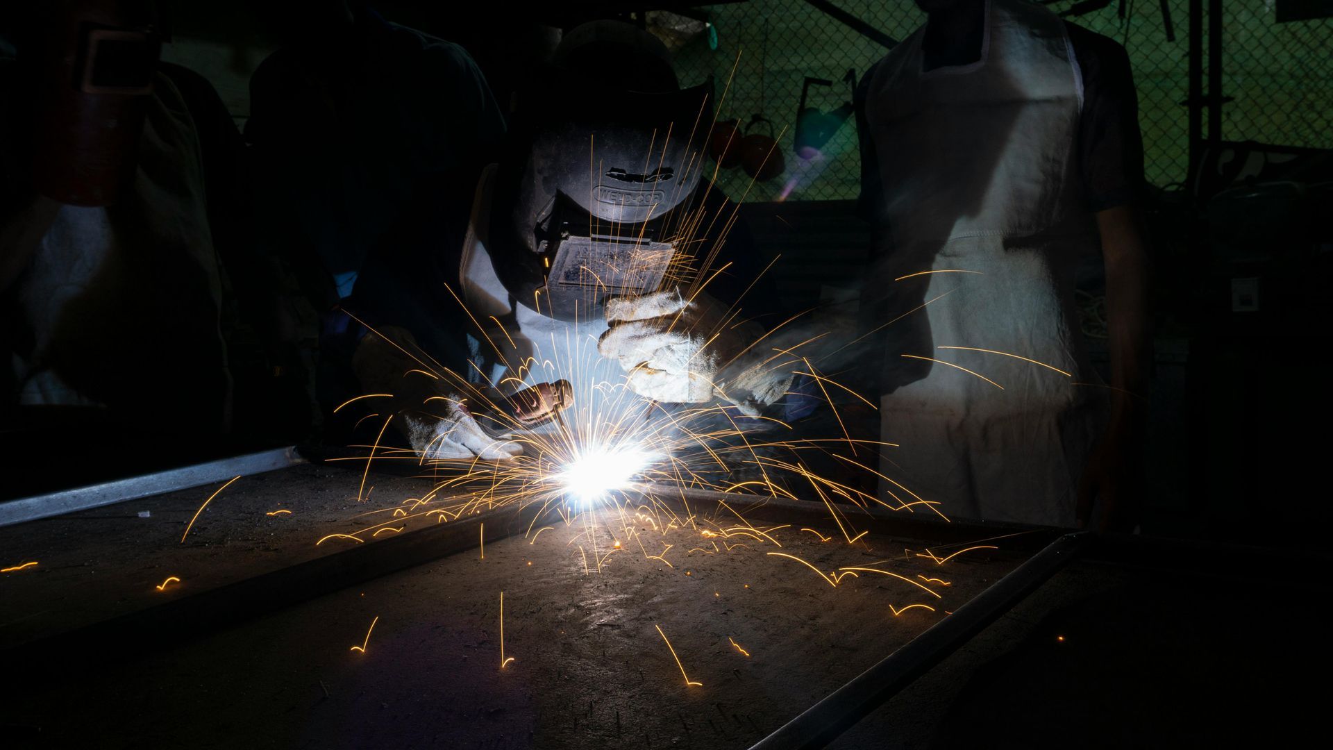 Welder creating bright sparks on a metal surface in a dark industrial workshop