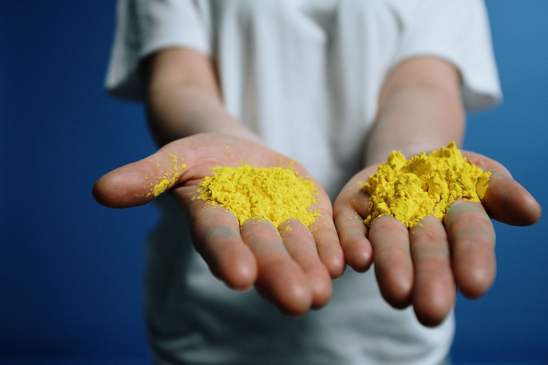 Hands holding two small piles of bright yellow powder against a blue background