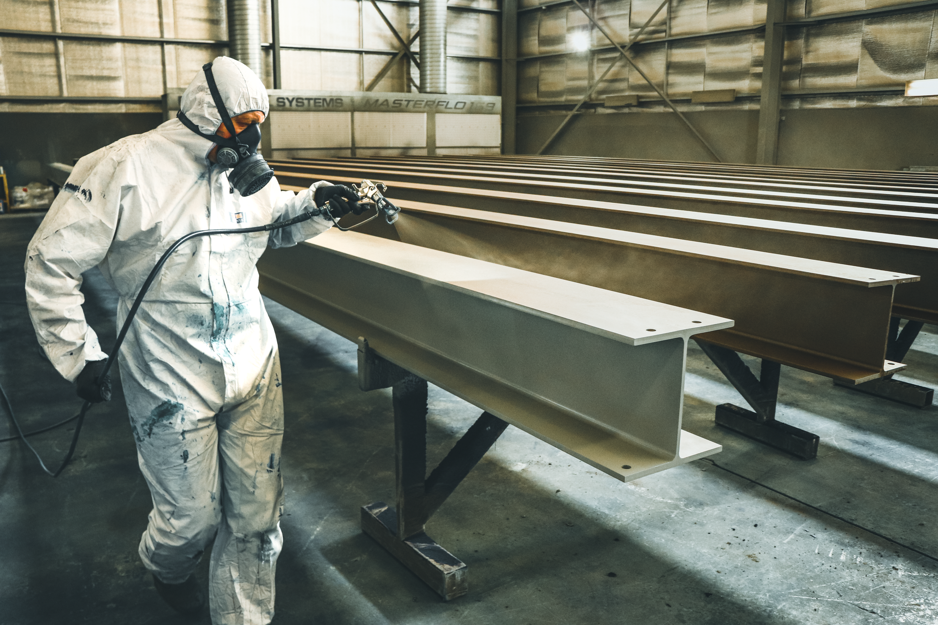 Worker in white protective suit inspecting metal beams in an industrial warehouse.