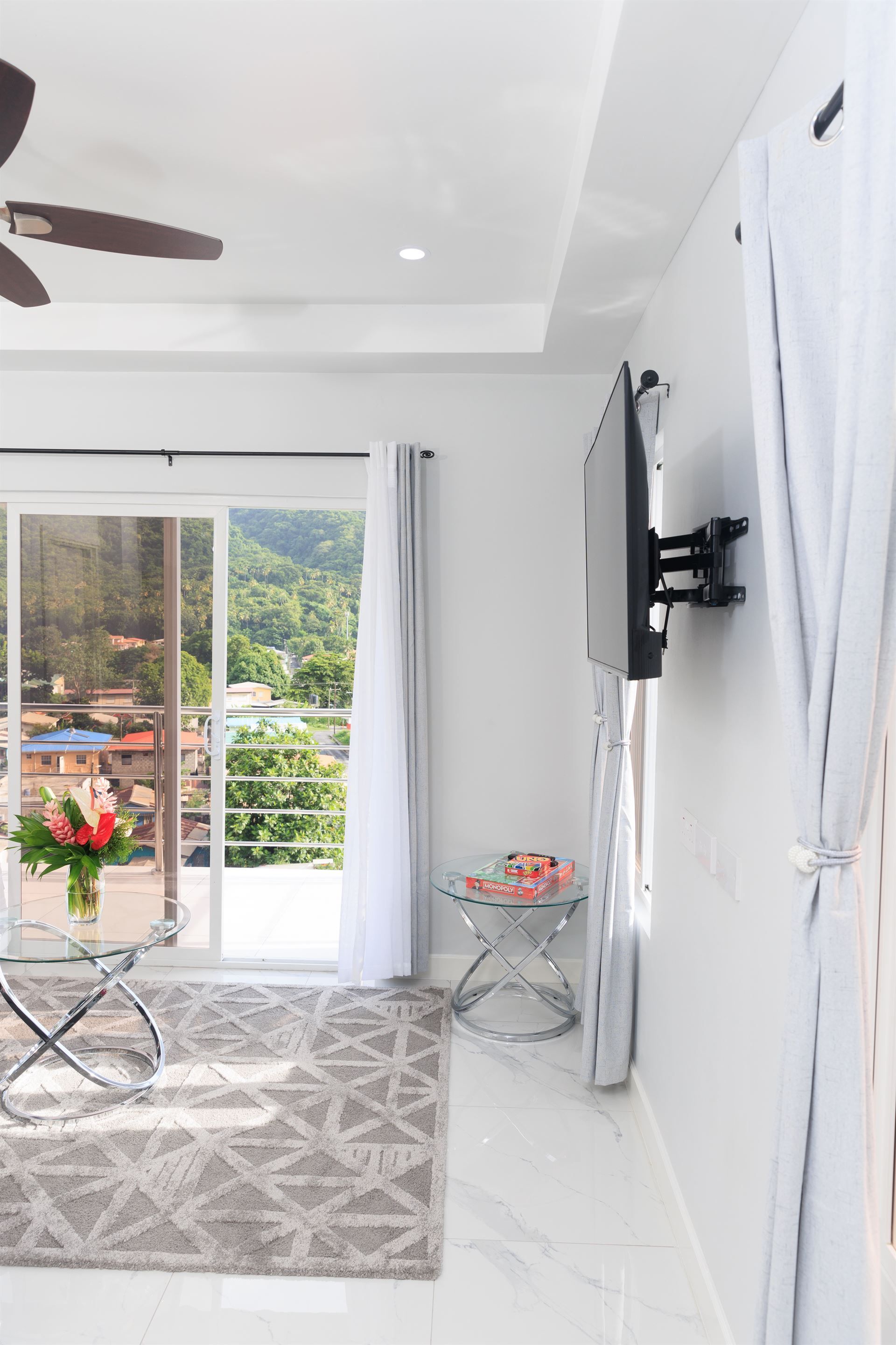 A living room with a ceiling fan and a flat screen tv mounted on the wall.