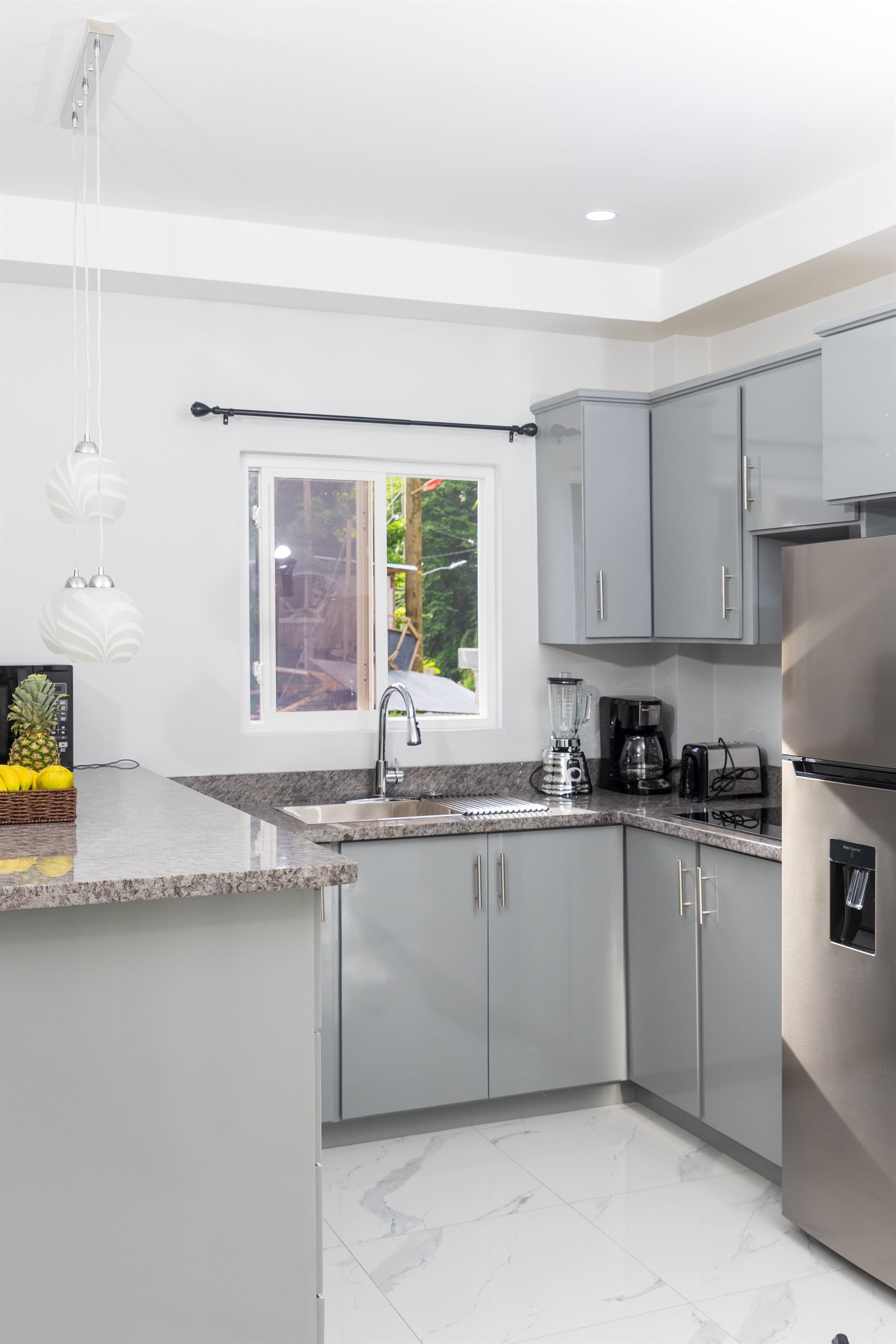 A kitchen with gray cabinets , a stainless steel refrigerator , a sink , and a window.