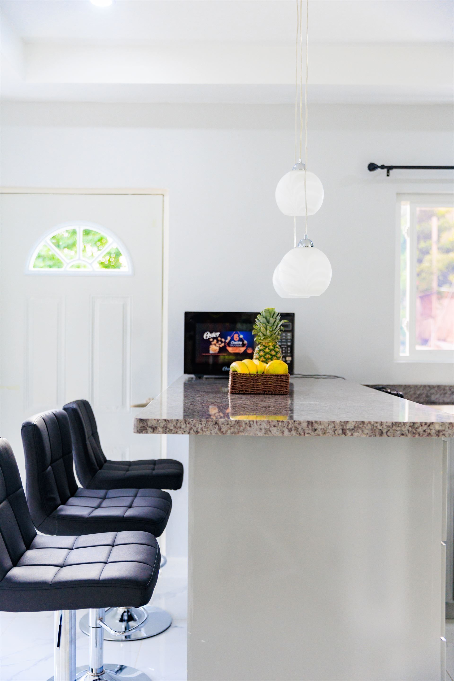 A kitchen with a bar and stools and a television on the counter.