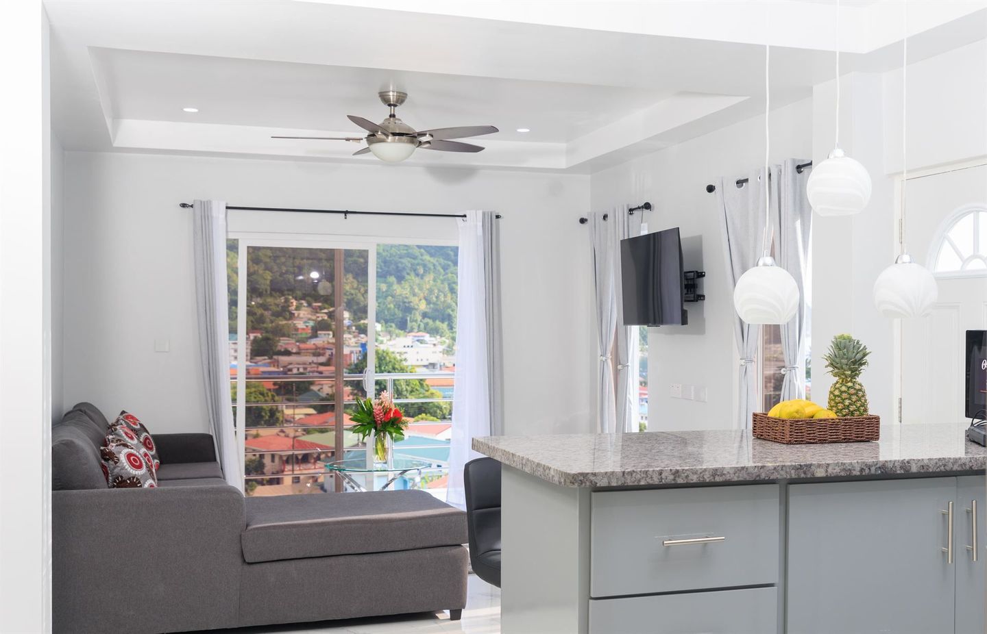 A living room with a couch and a kitchen with a ceiling fan.