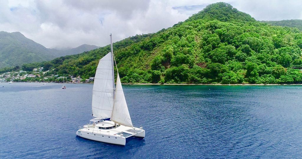 An aerial view of a sailboat in the ocean with mountains in the background.