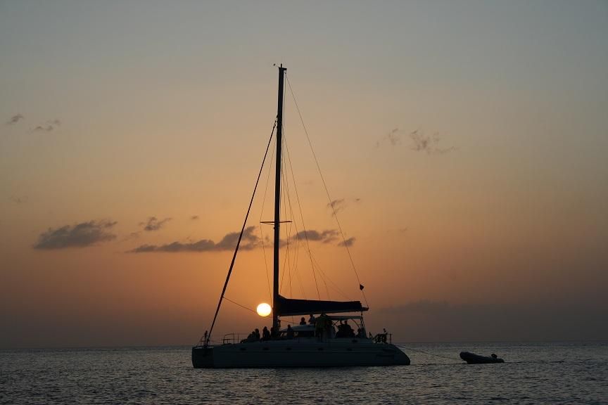 A sailboat is floating in the ocean at sunset.