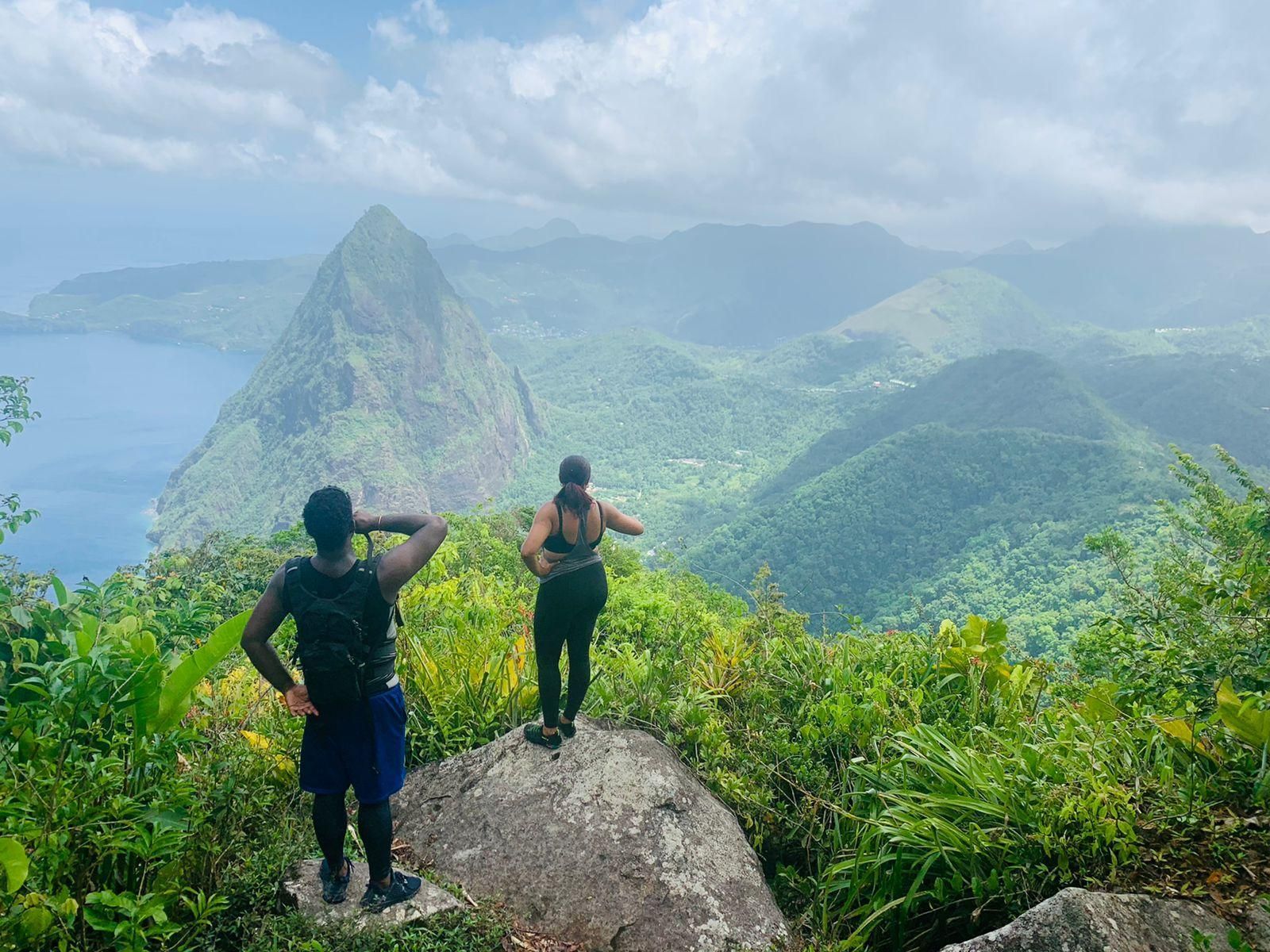 Two people are standing on top of a rock overlooking a mountain.