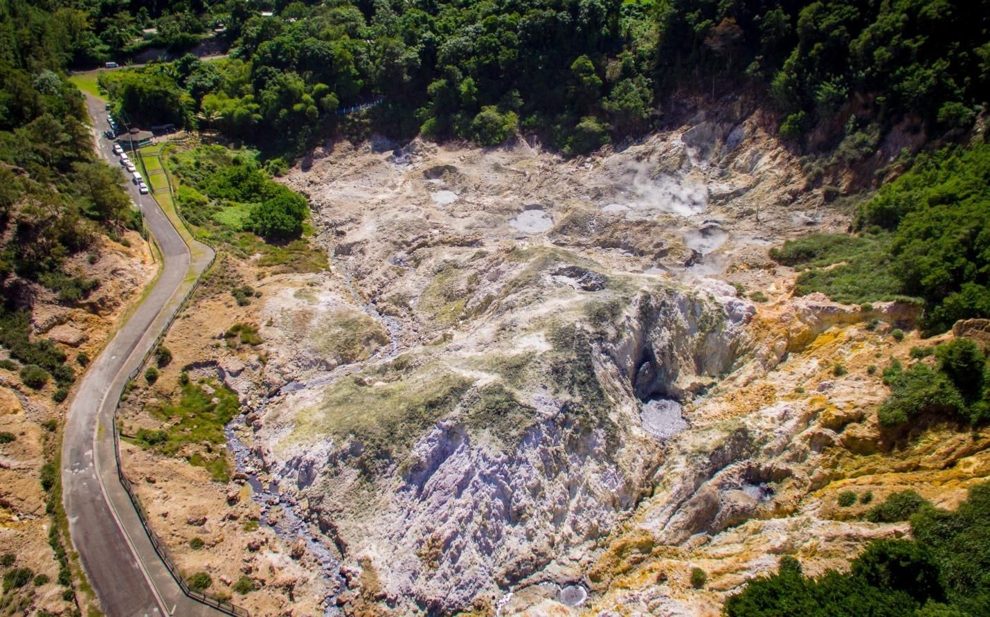 An aerial view of a road going through a mountainous area surrounded by trees.