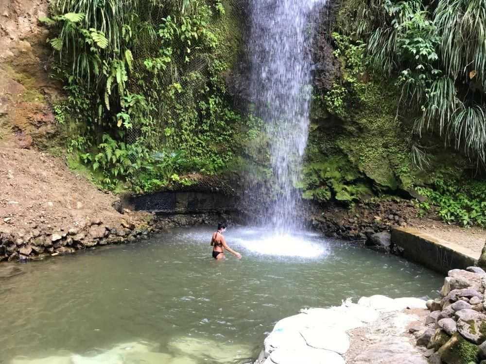 A woman is swimming in a pool under a waterfall.