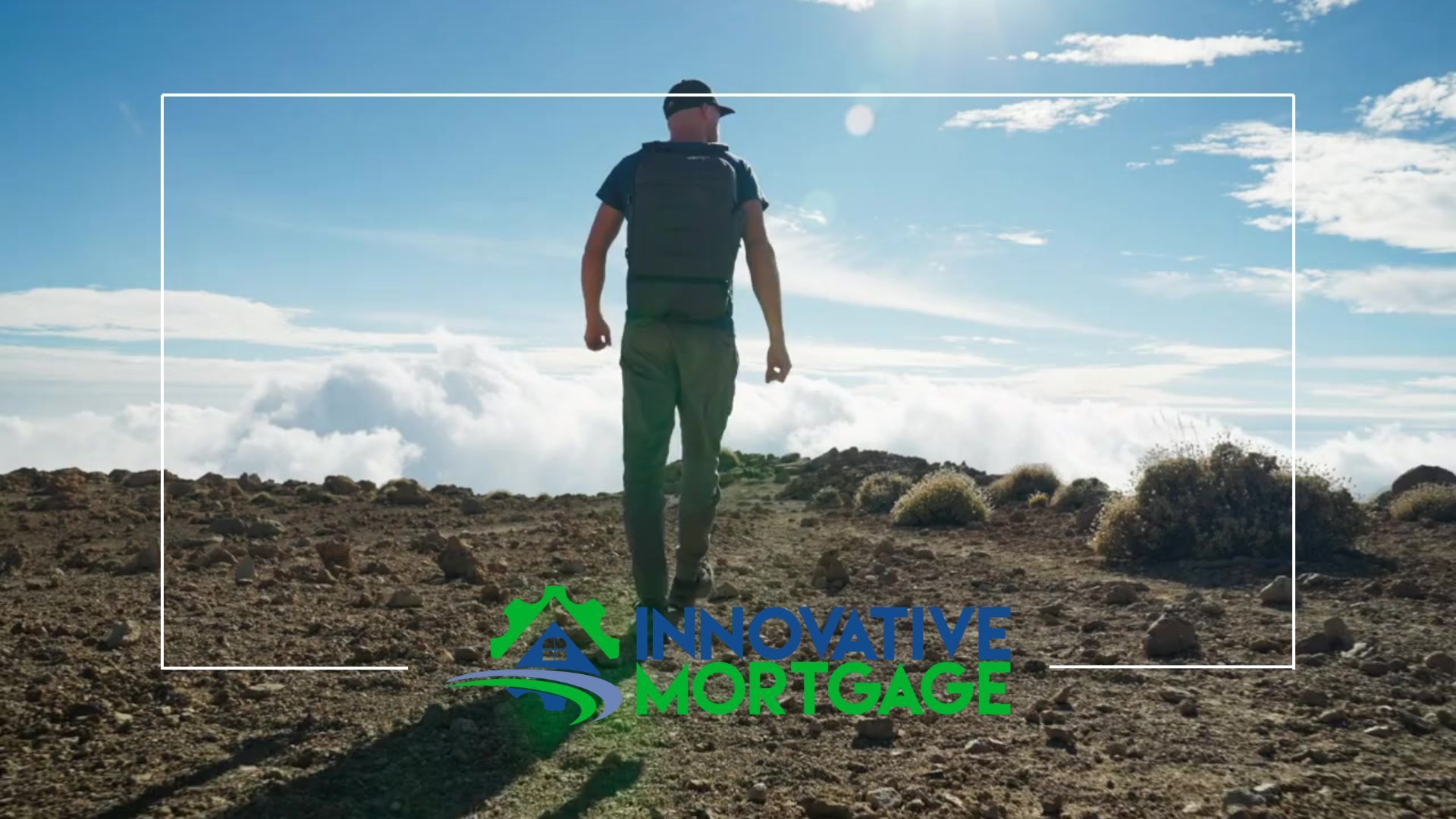 A man is standing on top of a mountain looking at the clouds.