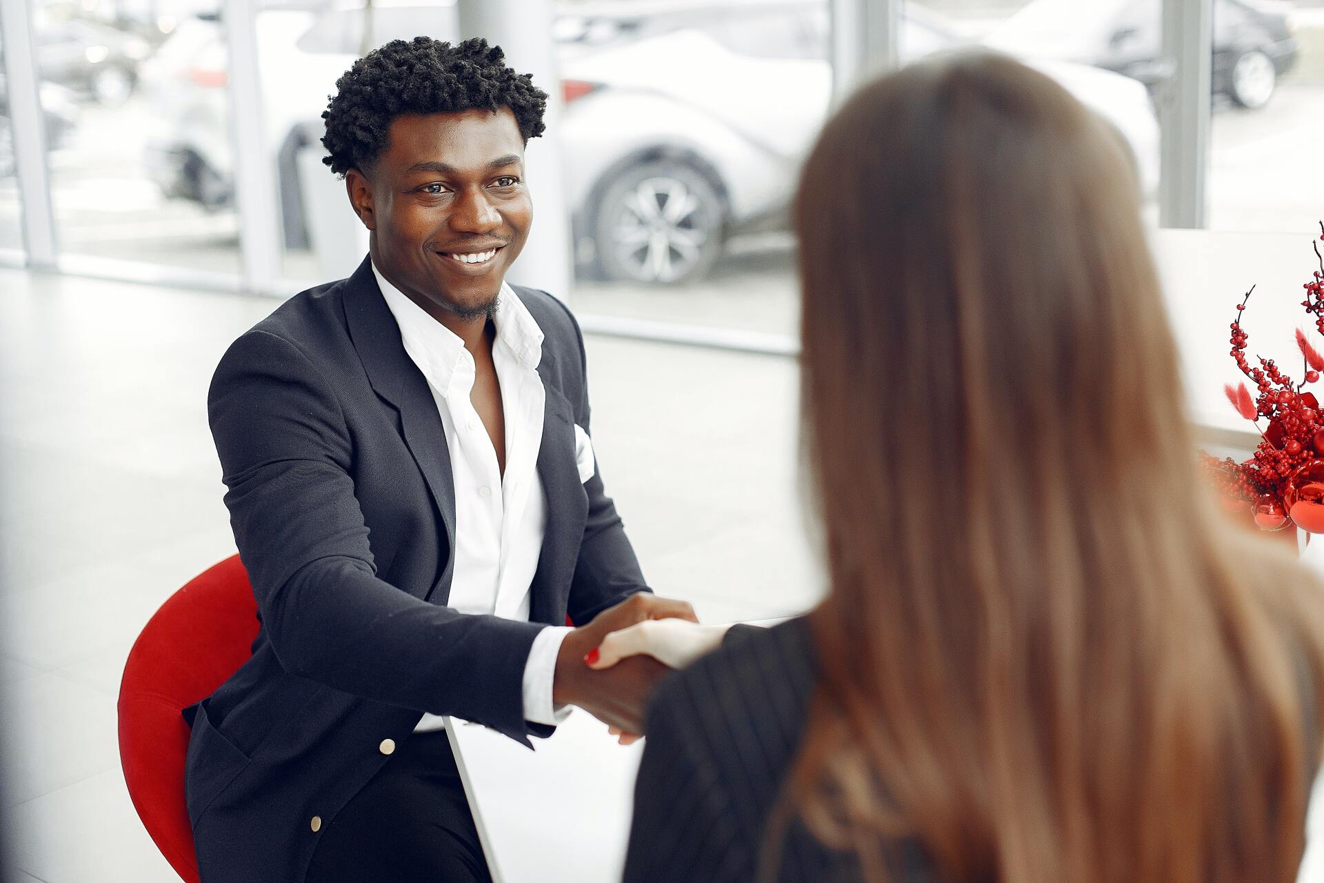 A man in a suit is shaking hands with a woman in a car showroom.