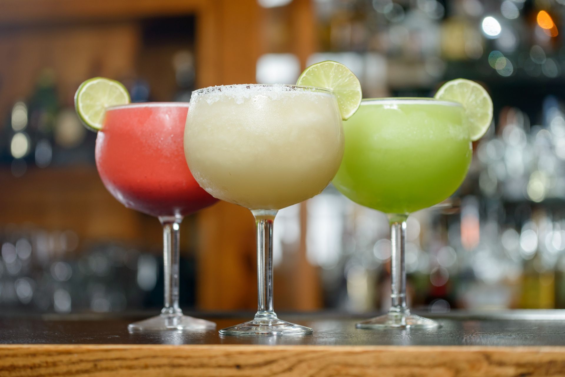 Three margaritas are sitting on a bar counter.