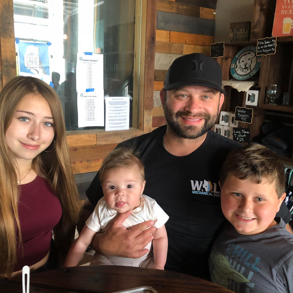 A man in a black shirt that says wol on it is holding a baby and two children