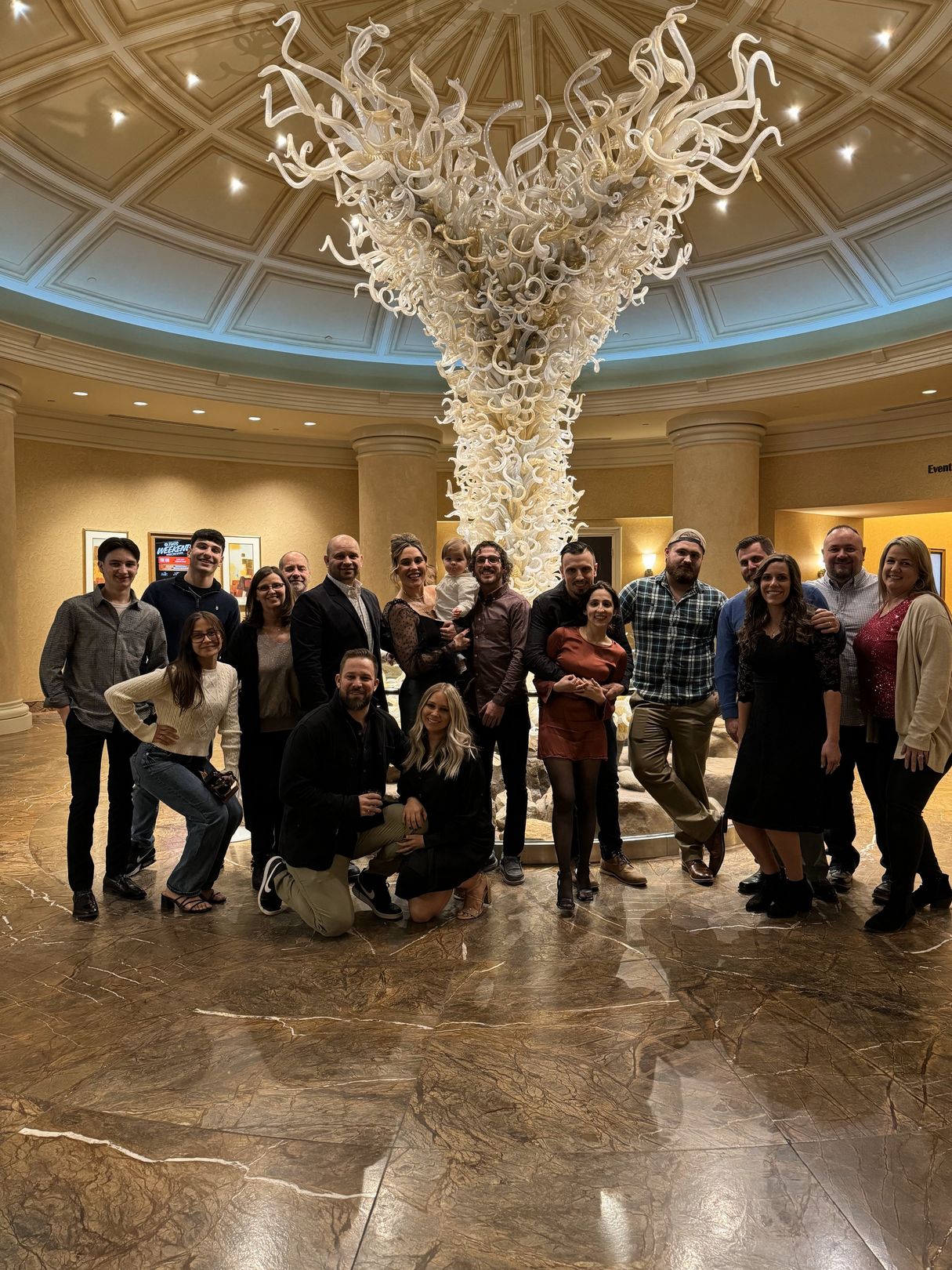 A group of people are posing for a picture in front of a large chandelier.