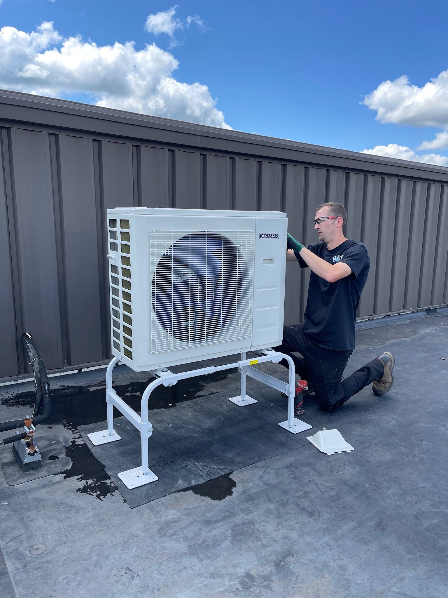 A man is working on an air conditioner on a roof.