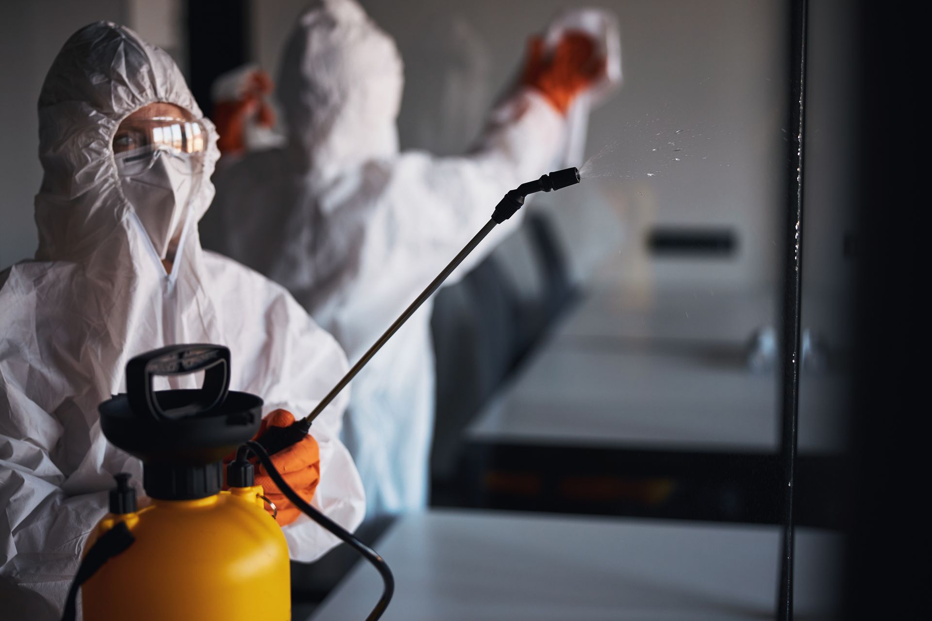 Un uomo con una tuta protettiva sta spruzzando una stanza con uno spruzzatore.