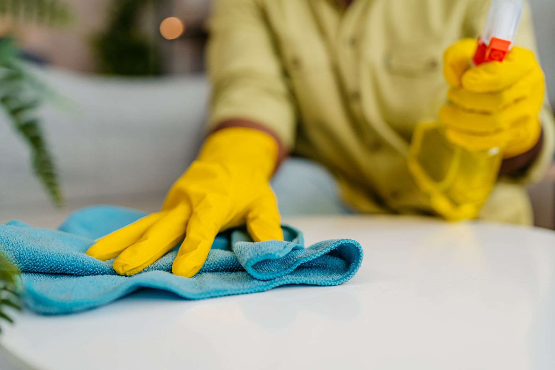 Una persona che indossa guanti gialli sta pulendo un tavolo con un panno e uno spruzzatore.