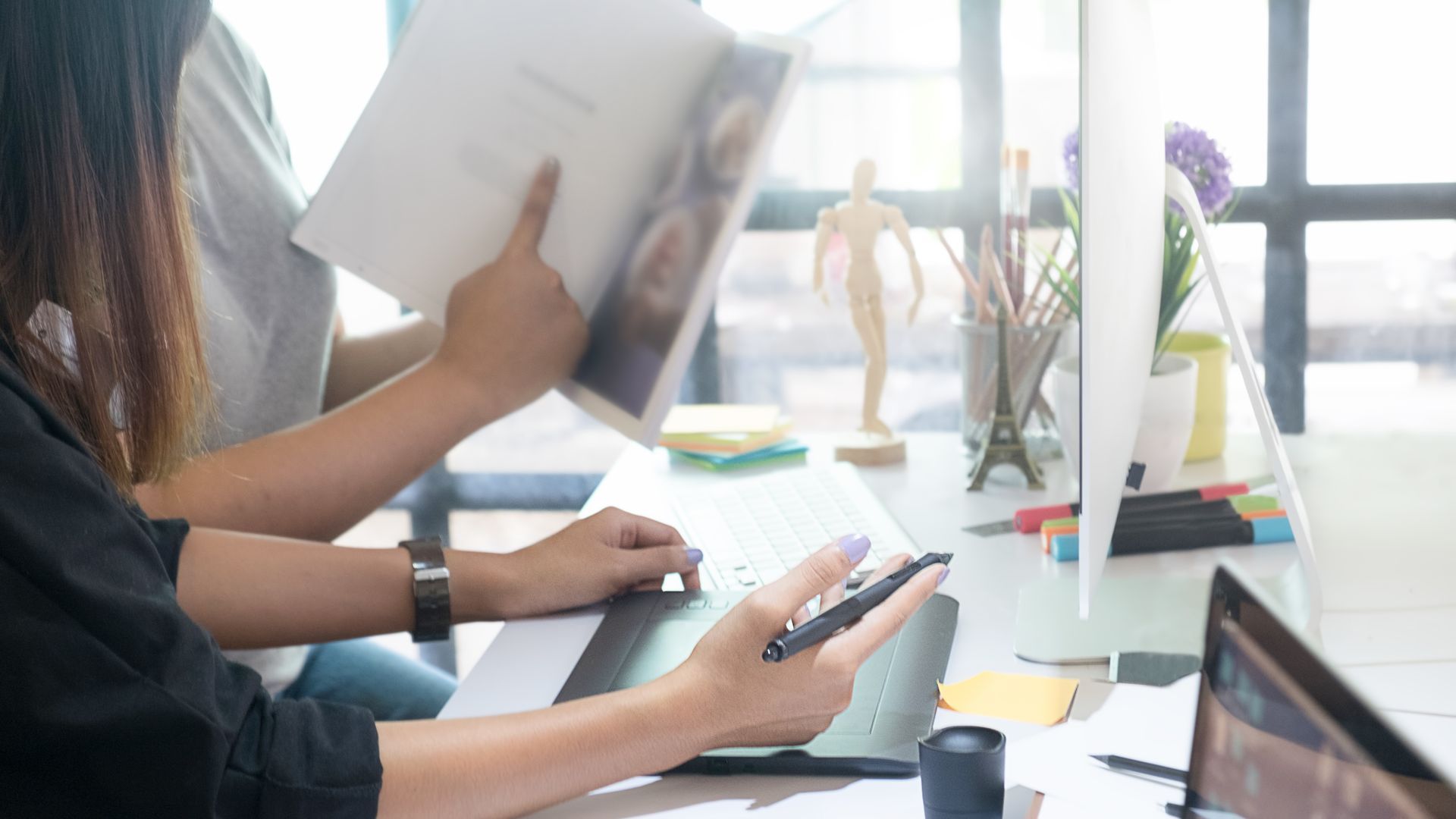 Deux collaborateurs à un bureau, l'un pointant un magazine du doigt, l'autre devant un ordinateur