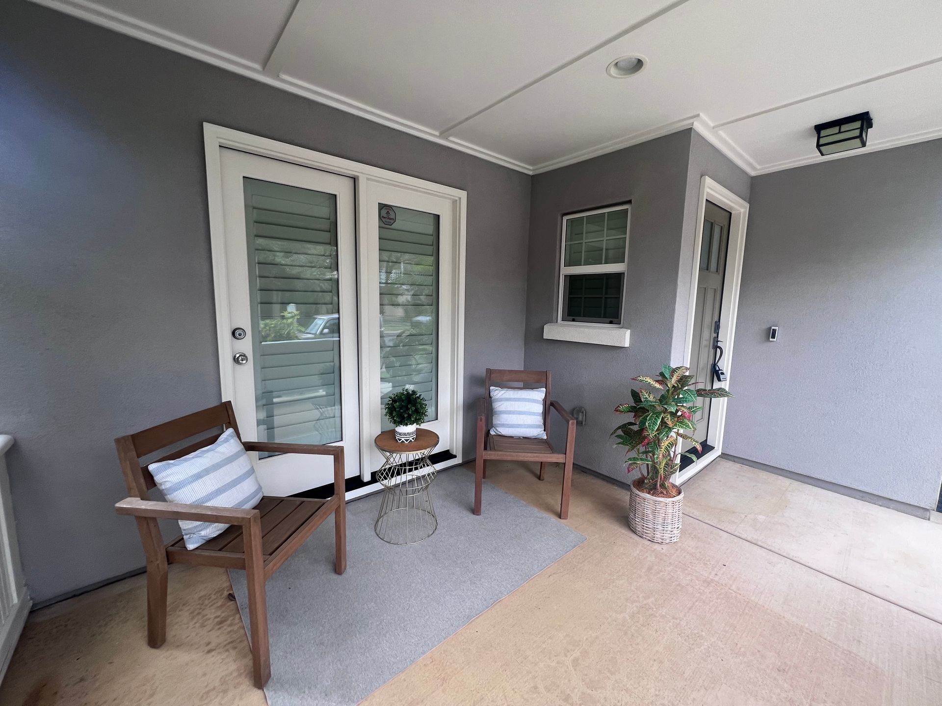 There are two chairs and a table on the porch of a house.