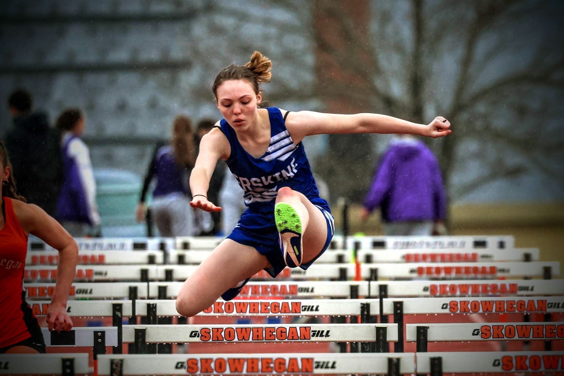 A female runner jumps over a hurdle that says arrowhead on it